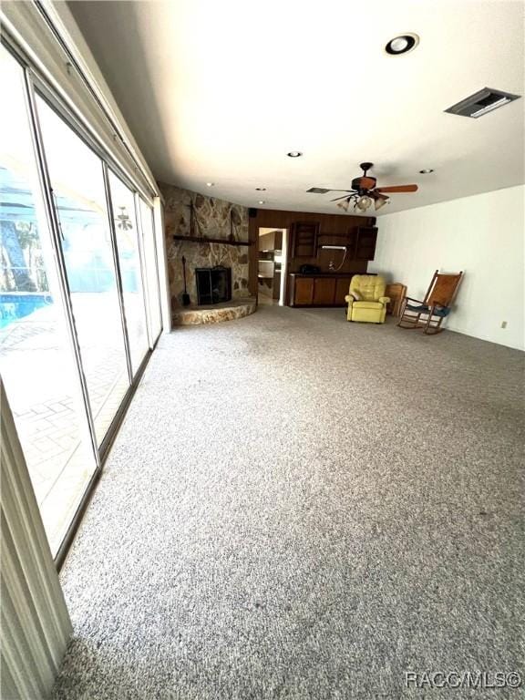 carpeted living room featuring ceiling fan and a stone fireplace