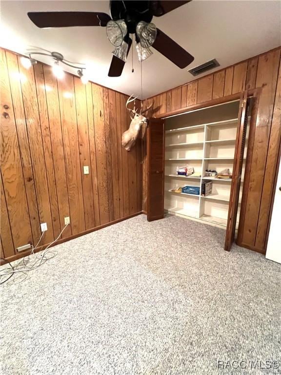 interior space featuring ceiling fan, wooden walls, and carpet