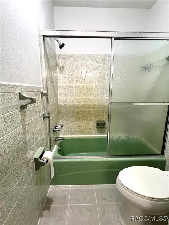 bathroom featuring tile walls, tile patterned flooring, enclosed tub / shower combo, and toilet