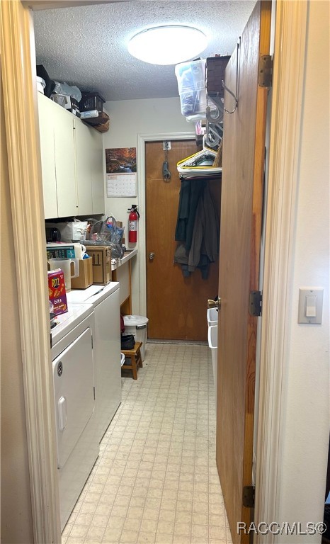 laundry area featuring cabinets, a textured ceiling, and washing machine and clothes dryer