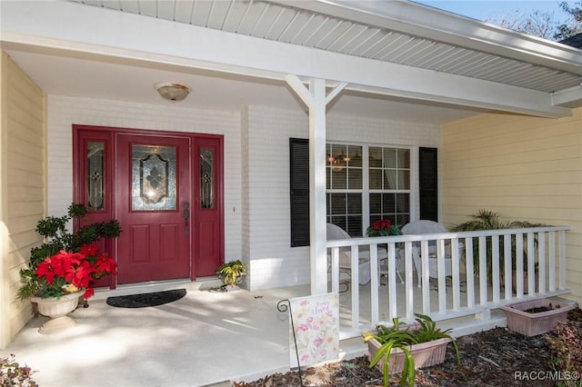 entrance to property featuring a porch and brick siding