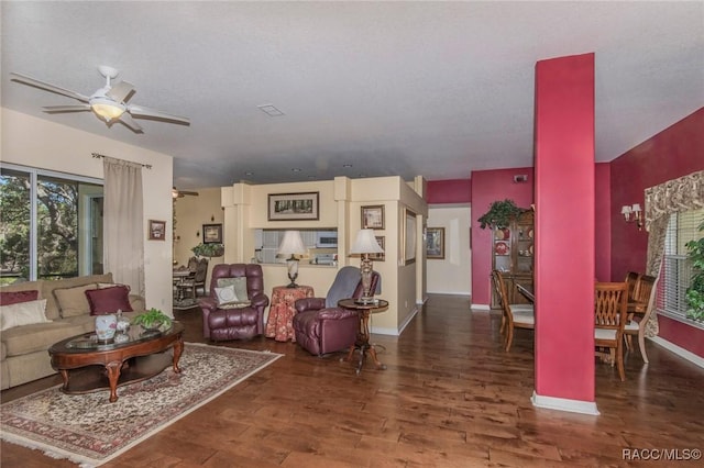 living area featuring ceiling fan, a textured ceiling, baseboards, and dark wood-type flooring