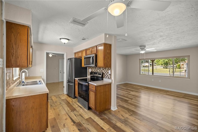 kitchen with sink, tasteful backsplash, light hardwood / wood-style flooring, appliances with stainless steel finishes, and ceiling fan