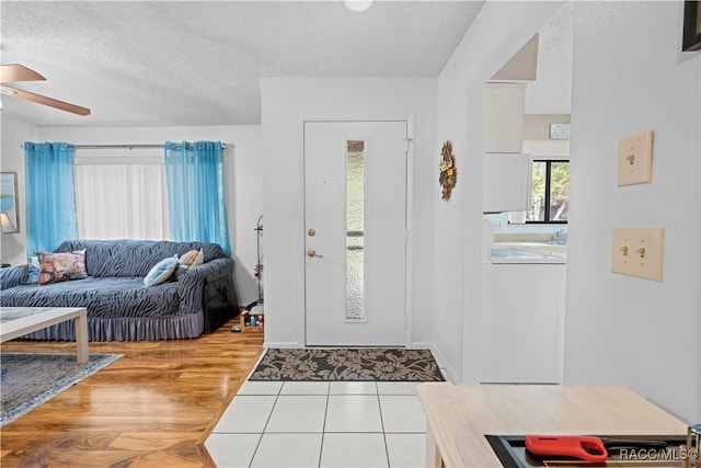 entrance foyer with washer / clothes dryer, a textured ceiling, ceiling fan, and light tile patterned floors