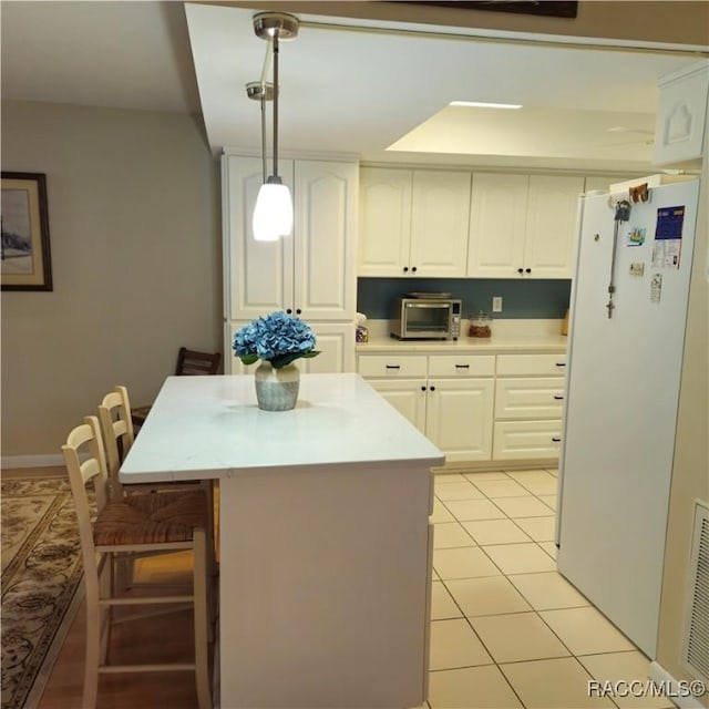 kitchen with white cabinetry, decorative light fixtures, white fridge, and light tile patterned floors