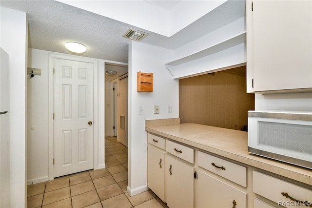 kitchen with light tile patterned floors, a textured ceiling, and white cabinetry