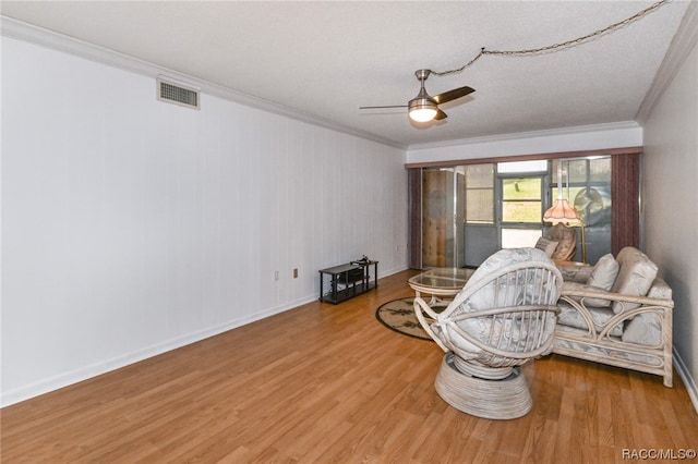 living area featuring hardwood / wood-style flooring, ceiling fan, ornamental molding, and a textured ceiling