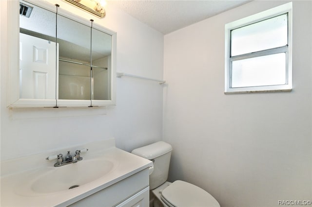 bathroom with a textured ceiling, vanity, toilet, and walk in shower