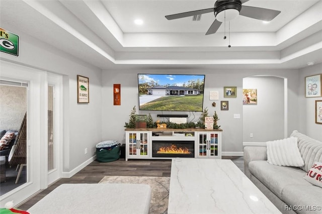 living room featuring a raised ceiling, baseboards, ceiling fan, and wood finished floors