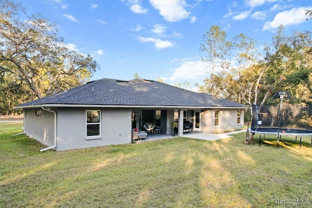 back of house with a trampoline, stucco siding, a patio, a yard, and roof with shingles
