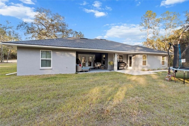 rear view of house with a trampoline, stucco siding, a patio, a yard, and french doors