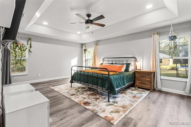 bedroom featuring a tray ceiling, wood finished floors, multiple windows, and recessed lighting