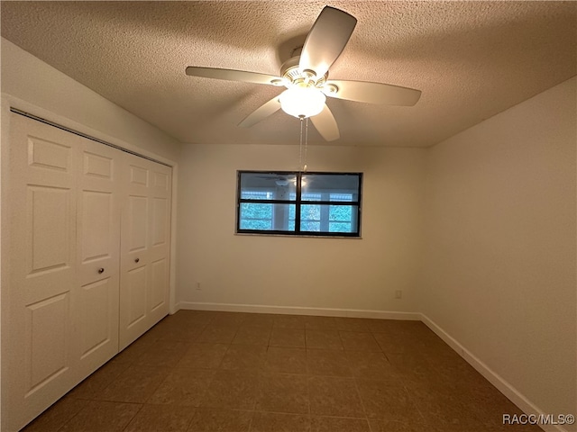 unfurnished bedroom with a textured ceiling, a closet, dark tile patterned flooring, and ceiling fan