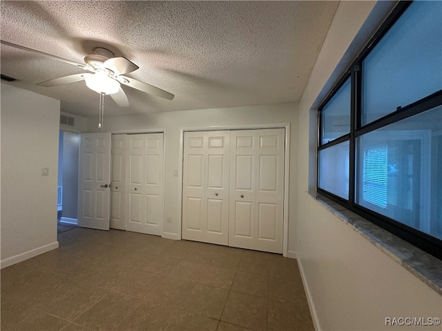 unfurnished bedroom with a textured ceiling, two closets, tile patterned floors, and ceiling fan