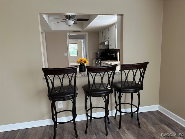 kitchen with ceiling fan, dark hardwood / wood-style flooring, kitchen peninsula, black / electric stove, and a kitchen bar