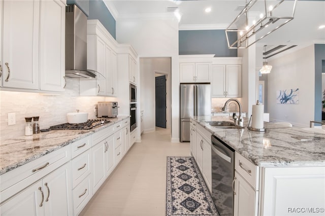 kitchen featuring appliances with stainless steel finishes, wall chimney exhaust hood, pendant lighting, white cabinetry, and an island with sink