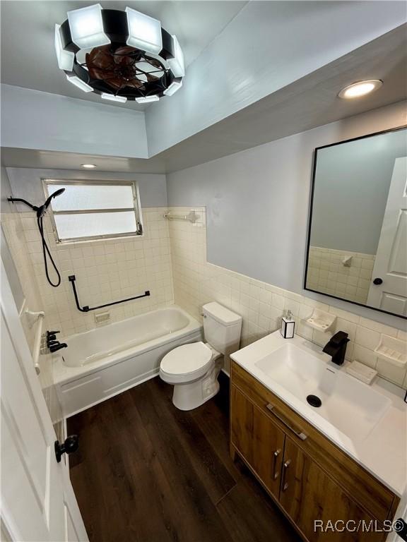 full bathroom with tiled shower / bath combo, wood-type flooring, toilet, vanity, and tile walls