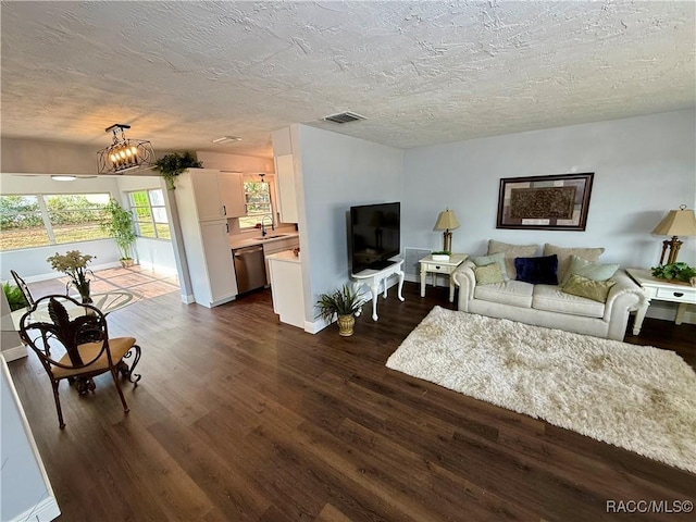 living room featuring a textured ceiling, dark hardwood / wood-style flooring, sink, and an inviting chandelier