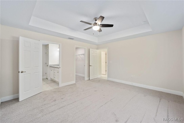 unfurnished bedroom with a raised ceiling, a spacious closet, and light carpet