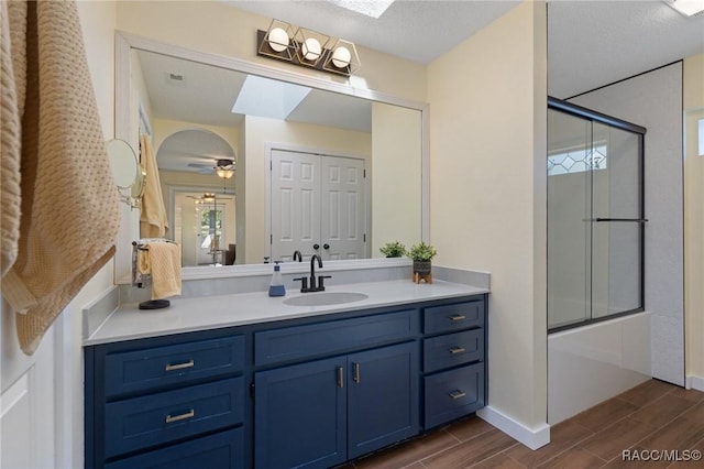 bathroom with a skylight, ceiling fan, a textured ceiling, shower / bath combination with glass door, and vanity