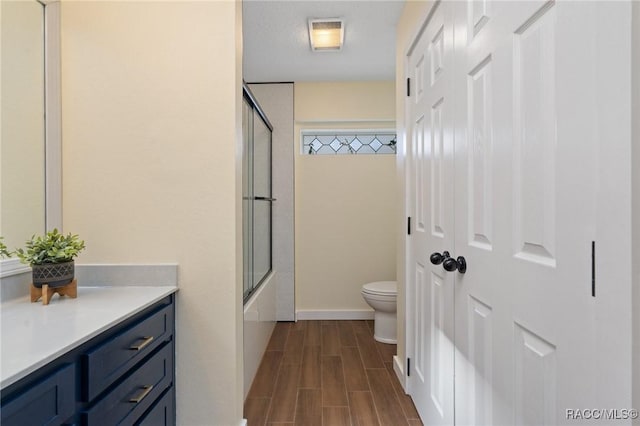 full bathroom featuring shower / bath combination with glass door, a textured ceiling, vanity, and toilet