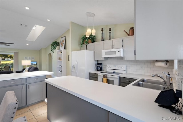 kitchen featuring white appliances, lofted ceiling with skylight, sink, hanging light fixtures, and tasteful backsplash