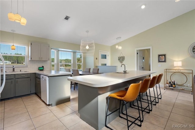 kitchen with light tile patterned flooring, backsplash, white dishwasher, hanging light fixtures, and a kitchen island