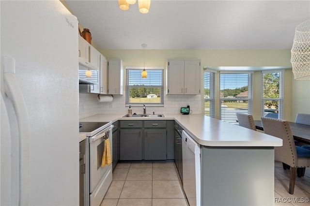 kitchen featuring kitchen peninsula, tasteful backsplash, white appliances, sink, and decorative light fixtures