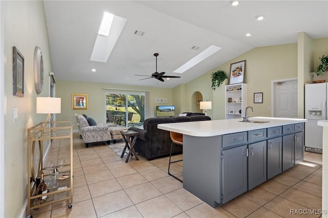 kitchen featuring white refrigerator with ice dispenser, a kitchen island with sink, sink, vaulted ceiling with skylight, and ceiling fan