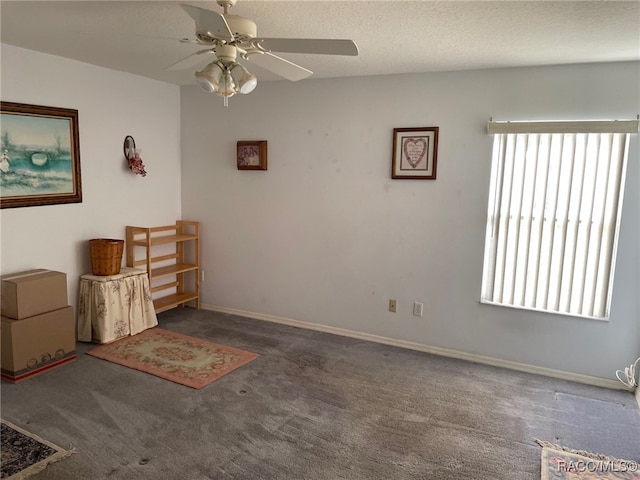 unfurnished room with a textured ceiling, dark carpet, and ceiling fan