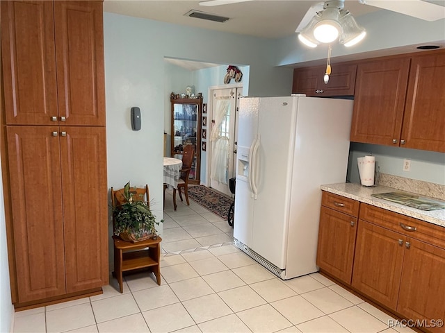 kitchen featuring white refrigerator with ice dispenser, light tile patterned floors, and light stone countertops