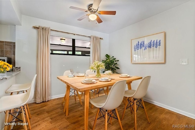 dining room with wood finished floors, a ceiling fan, and baseboards