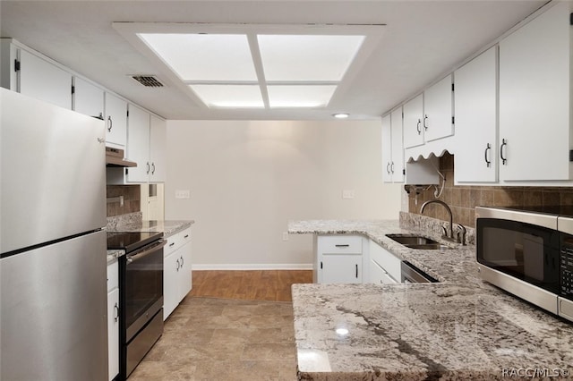 kitchen featuring appliances with stainless steel finishes, white cabinetry, a sink, light stone countertops, and under cabinet range hood