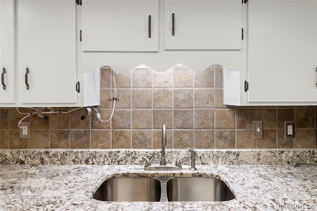 kitchen featuring decorative backsplash, a sink, light stone counters, and white cabinets