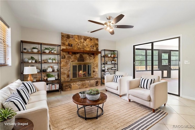 living room featuring a ceiling fan, a stone fireplace, and light tile patterned floors