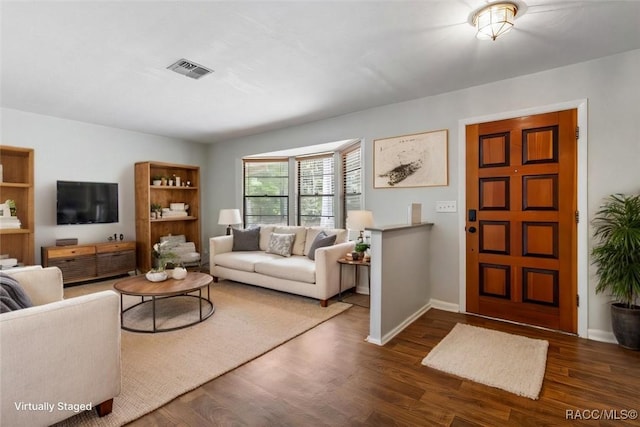 living area featuring dark wood-style flooring, visible vents, and baseboards