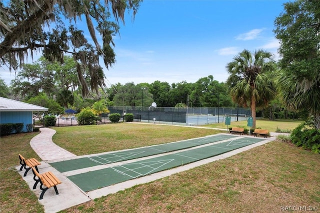 view of home's community featuring shuffleboard, a lawn, fence, and a tennis court