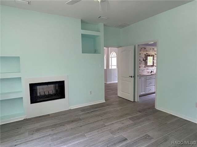 5774 N Lamp Post Dr, Beverly Hills, FL 34465 - unfurnished living room with wood finished floors, a ceiling fan, a multi sided fireplace, and built in features