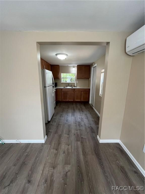 kitchen with an AC wall unit, dark wood-type flooring, sink, and white fridge