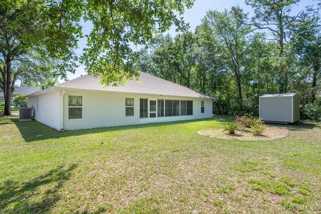 rear view of property with stucco siding, central AC unit, an outbuilding, a lawn, and a storage unit