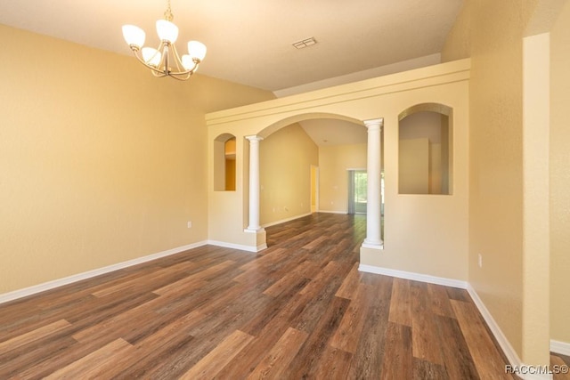 spare room featuring a chandelier, arched walkways, decorative columns, and wood finished floors