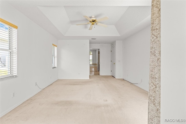 carpeted spare room featuring ceiling fan, a healthy amount of sunlight, and a tray ceiling