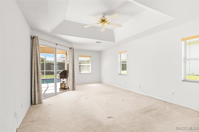 empty room featuring light carpet, a raised ceiling, ceiling fan, and a healthy amount of sunlight