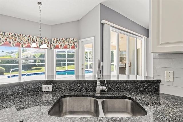 kitchen with sink, hanging light fixtures, dark stone countertops, decorative backsplash, and white cabinets