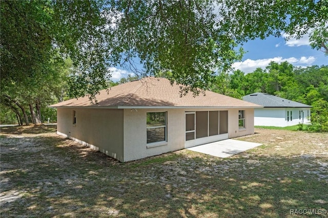 back of property with roof with shingles, stucco siding, and a sunroom