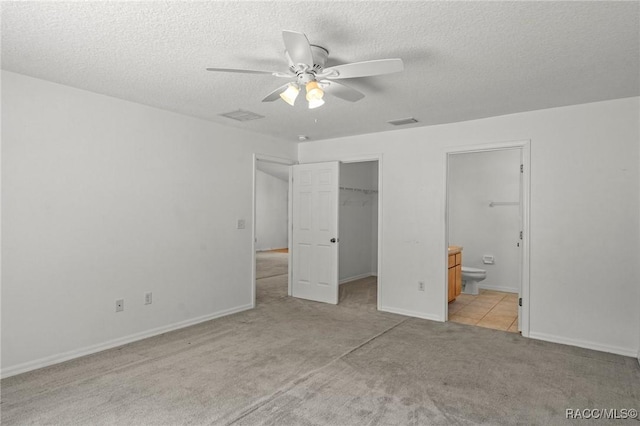 unfurnished bedroom featuring a closet, light carpet, ensuite bathroom, a walk in closet, and a textured ceiling