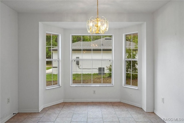 unfurnished dining area featuring plenty of natural light, baseboards, tile patterned floors, and a chandelier