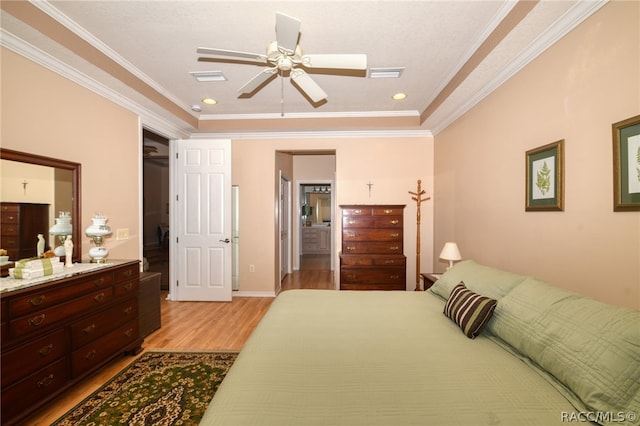 bedroom with light hardwood / wood-style floors, ceiling fan, ornamental molding, and a tray ceiling