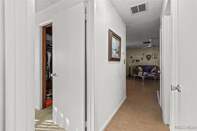 corridor with light tile patterned flooring, visible vents, a textured ceiling, and baseboards