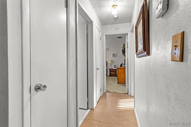 hall with light tile patterned floors, visible vents, a textured ceiling, and a textured wall